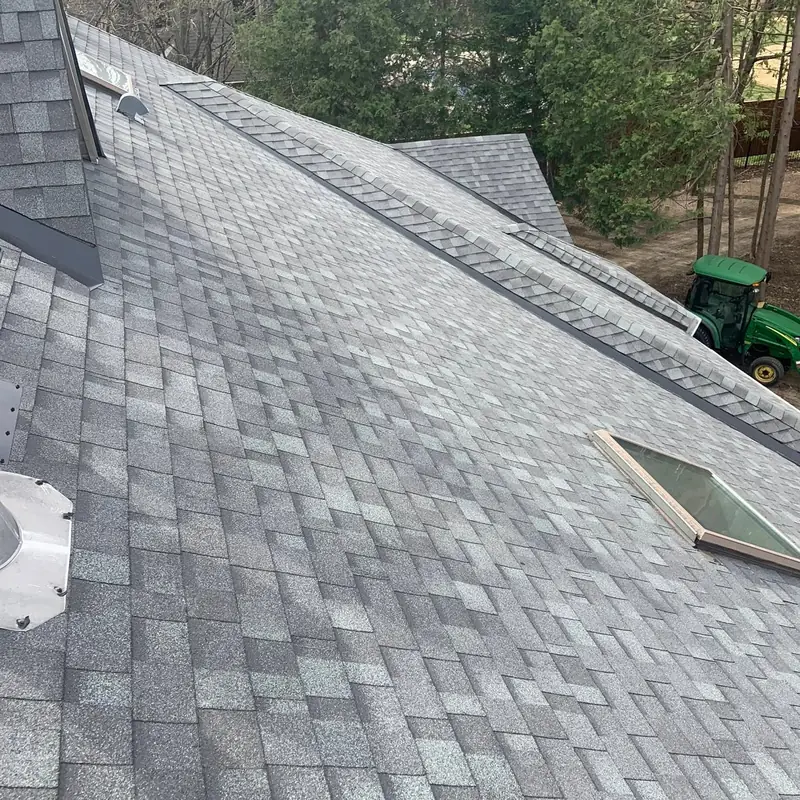 Long shingled roof slope with a skylight and ridge vent, green tractor at the bottom
